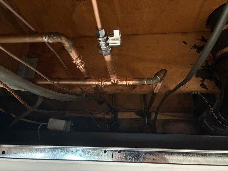 Responded to service call for refrigerator water line dispensing hot water and potential dishwasher leak. Upon inspection, accessed plumbing connections beneath kitchen cabinetry and identified refrigerator supply line cross-connected to hot water supply instead of cold water line. Documented existing copper piping configuration, brass fittings, and appliance connections. Assessed dishwasher installation and surrounding plumbing infrastructure for signs of active leakage. Photographed plumbing layout including supply lines, shut-off valves, and connection points for service documentation and repair planning purposes.
