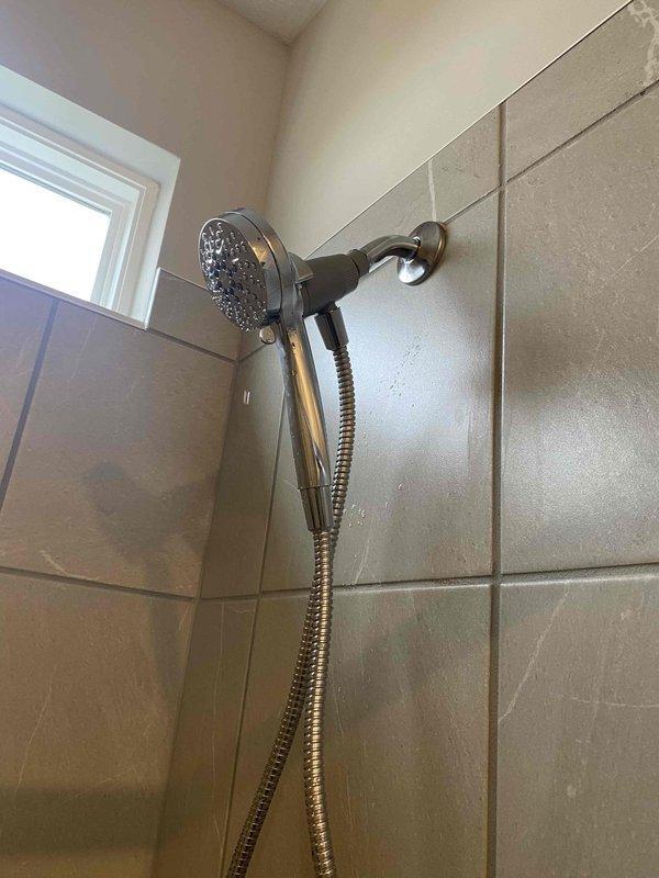 Completed installation of Chrome Moen Magnetix handheld showerhead system as a return service call. The new fixture was mounted to the existing shower arm with proper sealing, featuring a chrome finish spray head connected via flexible metal hose to a wall-mounted holder with oil-rubbed bronze finish. System was tested for proper water flow and functionality, with no leaks detected at connection points.
