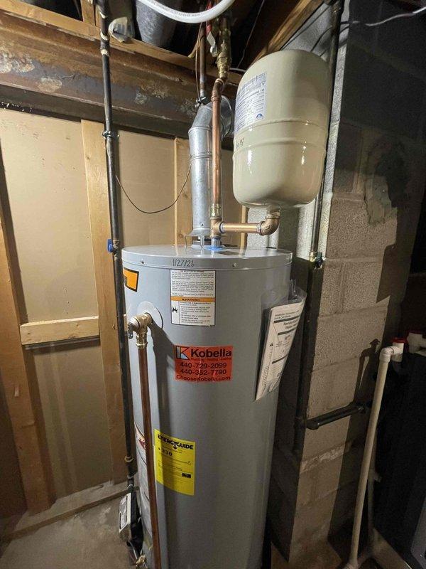 Successfully installed a Kobella tanked water heater in basement utility area as a return service. Installation included proper connection of copper inlet/outlet pipes, mounting of expansion tank, and connection of metal ventilation ducting. System includes DEFENDER safety features and all necessary valves, with all components securely mounted to the wall structure.
