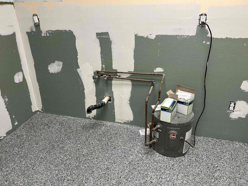 Conducted estimate for replacement of two bathroom faucets, two toilets, and one kitchen faucet in an unoccupied office space under renovation. Observed walls in various stages of preparation with plumbing rough-ins visible, including drain fittings and water supply pipes. Noted existing Rheem water heater with copper supply lines that will need to be connected to new fixtures once installed.