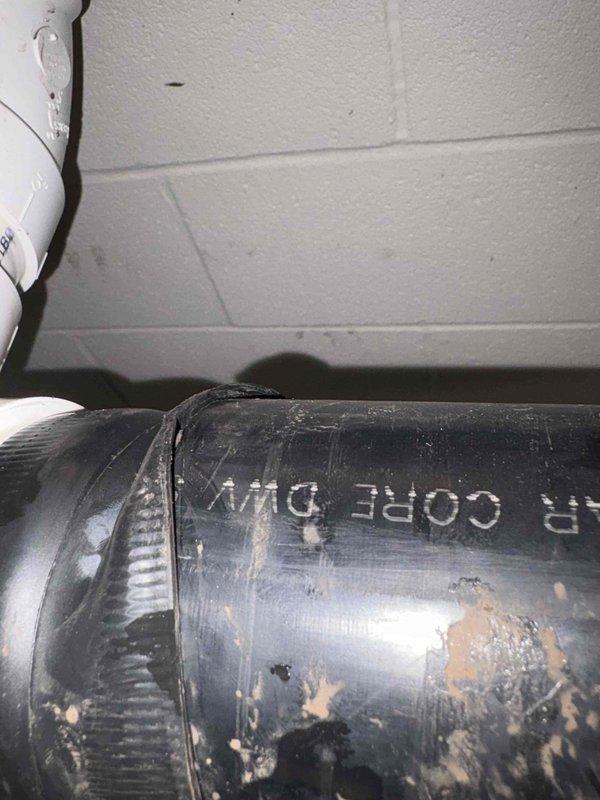Responded to callback for water leakage from drainage pipe onto shelving unit. Upon inspection, verified the black CORE DWV (Drain-Waste-Vent) flexible pipe installation for proper pitch and alignment using a spirit level. Examined pipe connections and clamping points where sections join together against the foundation wall. Documented existing conditions showing visible wear, debris accumulation, and potential points of water seepage on the corrugated drainage line. Assessed the horizontal run of the DWV pipe secured to ceiling joists above the affected area to identify source of dripping water reported by customer.